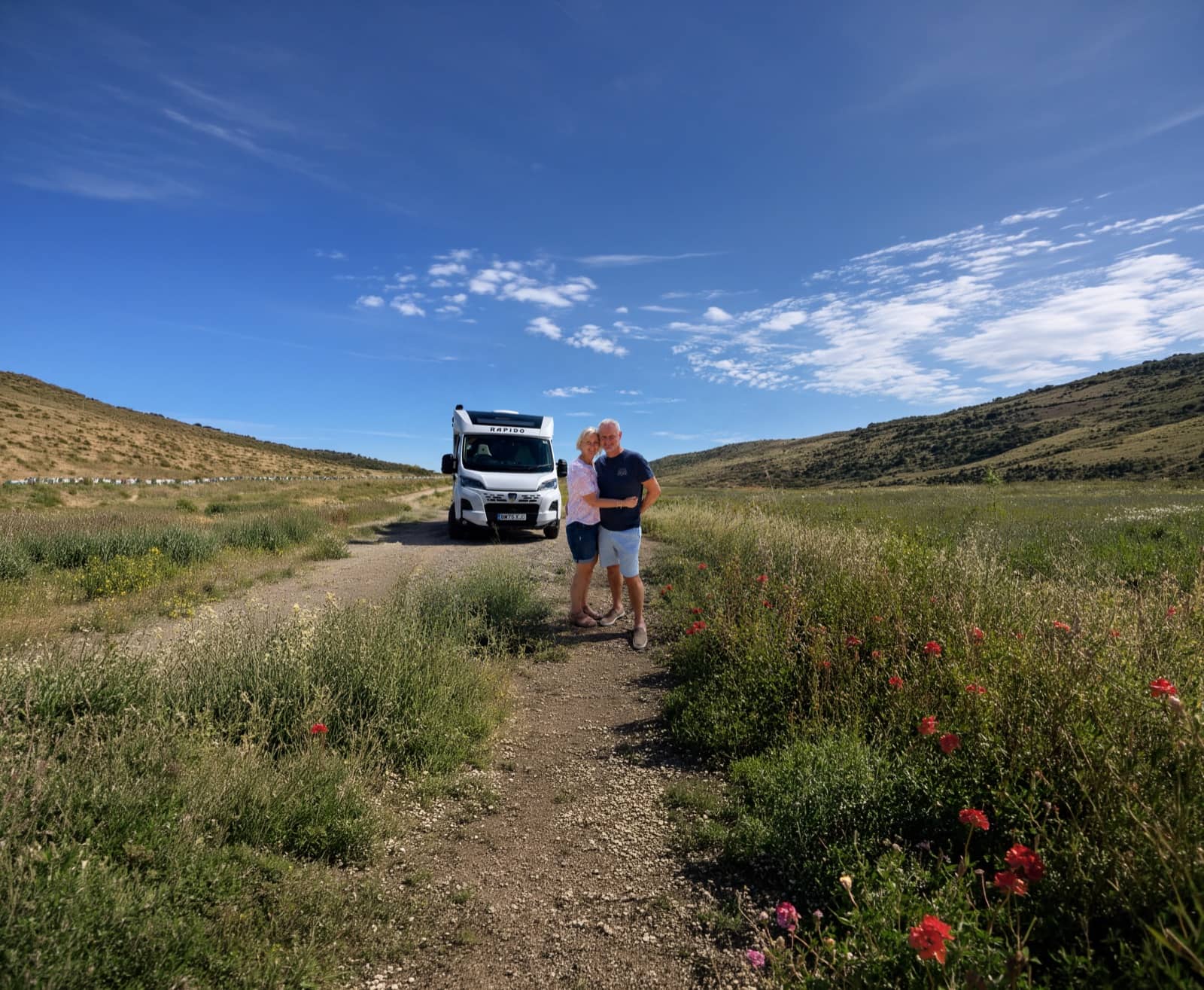 Et par, der står ved siden af deres autocamper på en sti gennem grønne, bakkede landskaber