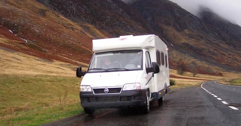Autocamper, der kører på en våd vej gennem tågede bakker