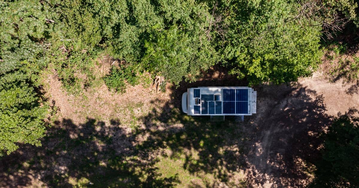 Luftfoto af en autocamper med tagmonterede solpaneler parkeret i en skovlysning