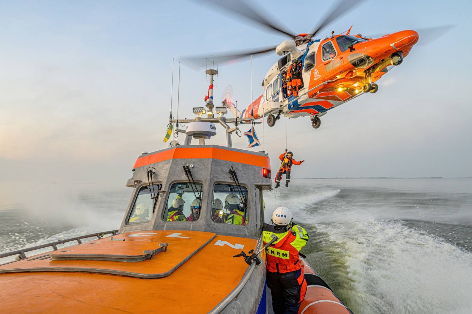 KNRM-redningsfartøj på havet med en redningshelikopter, der hejser et besætningsmedlem op