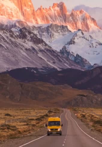Gul autocamper på en åben vej under det sneklædte Fitz Roy-massiv i Patagonien